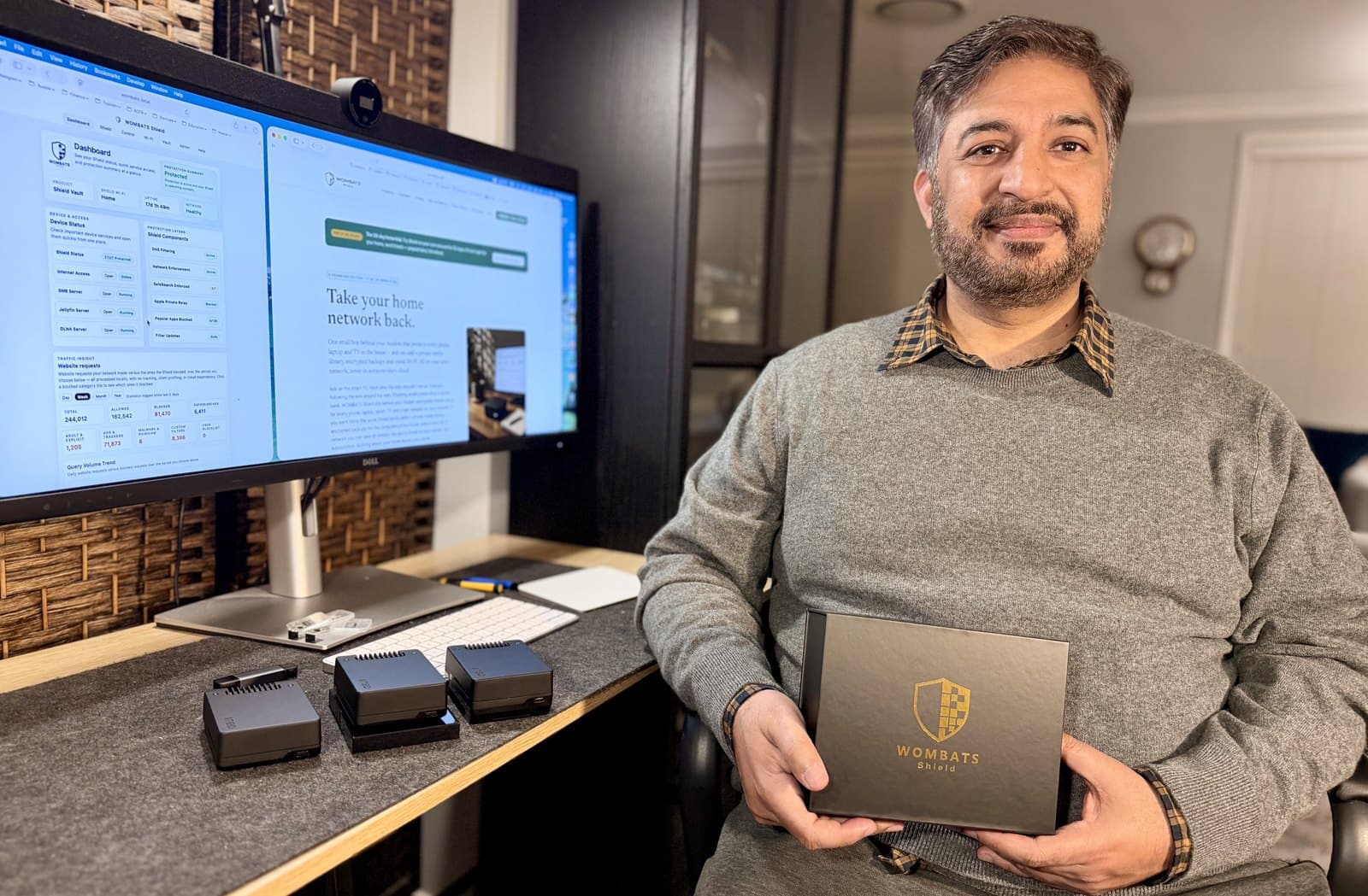 Khalid, founder of WOMBATS Shield, at his desk with a Shield device on the table and the dashboard on the monitor.