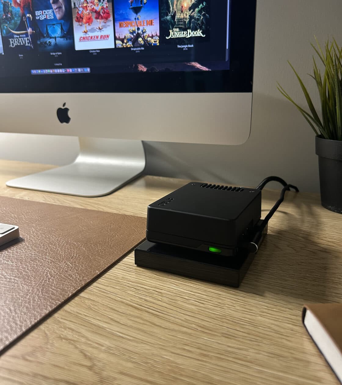 Shield Edge sitting on top of the household's own hard drive — the two-piece stack — green status light on, with the family film library open on the iMac behind it.